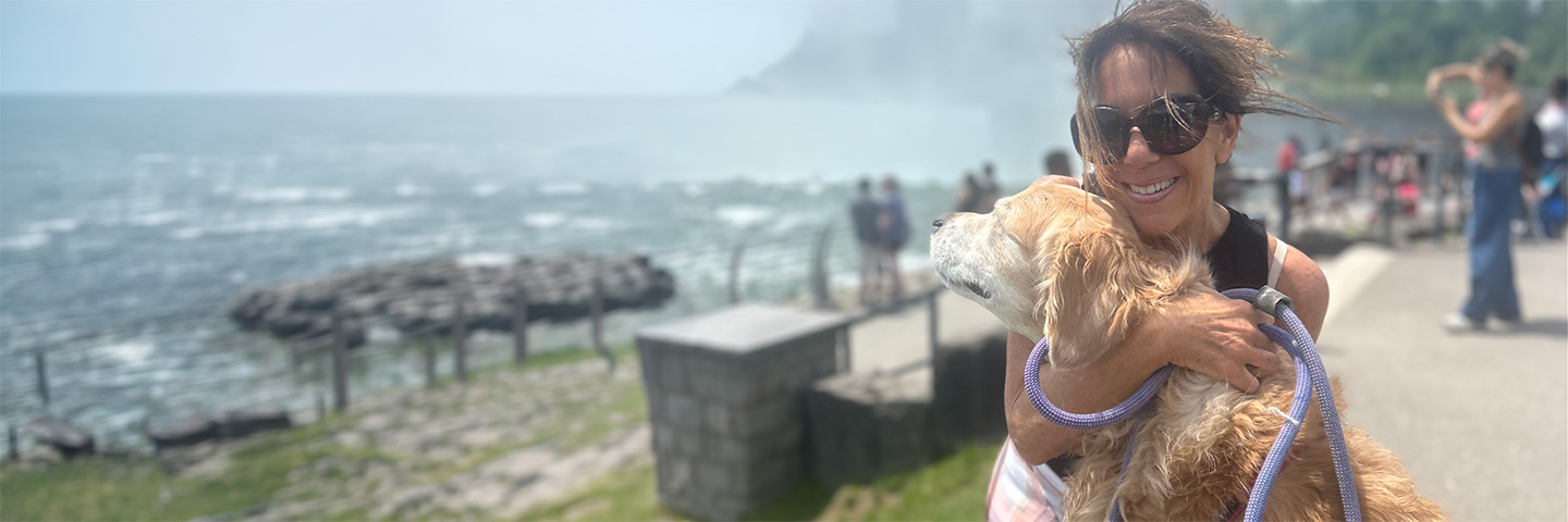 Caren Corso smiling and hugging her golden retriever at a waterfall overlook.