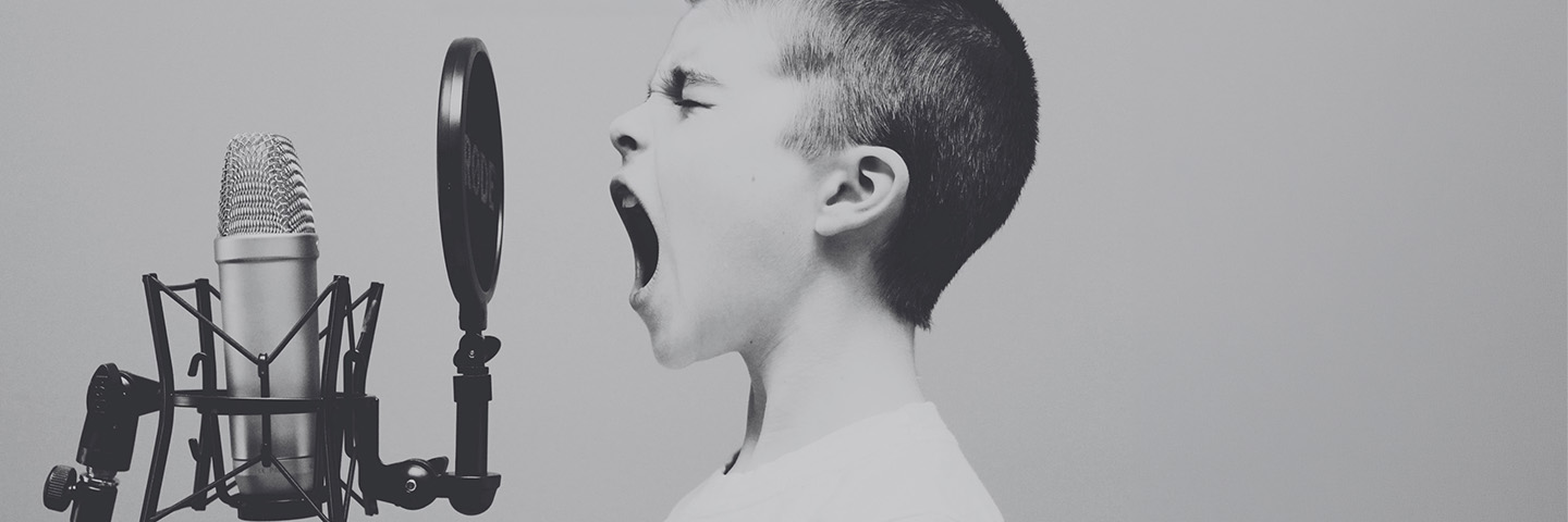 A boy shouting into a studio microphone with a pop filter.